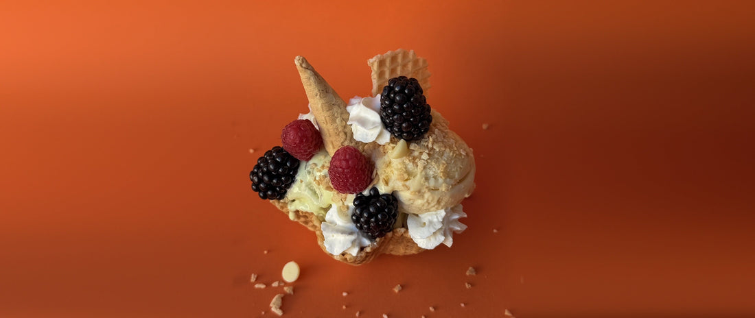 Waffle bowl sundae with vanilla and pistachio ice cream, blackberries, raspberries, whipped cream and wafer pieces on an orange background