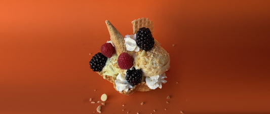 Waffle bowl sundae with vanilla and pistachio ice cream, blackberries, raspberries, whipped cream and wafer pieces on an orange background